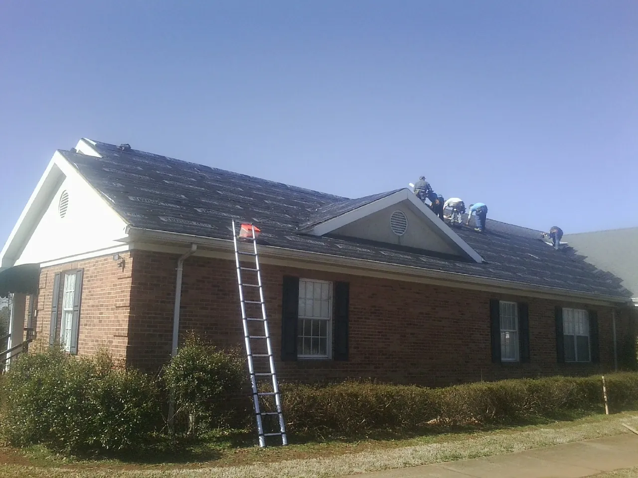 Crew tearing shingles off a brick ranch roof with a ladder set — Emergency Roof Repair work by our crew in El Cajon