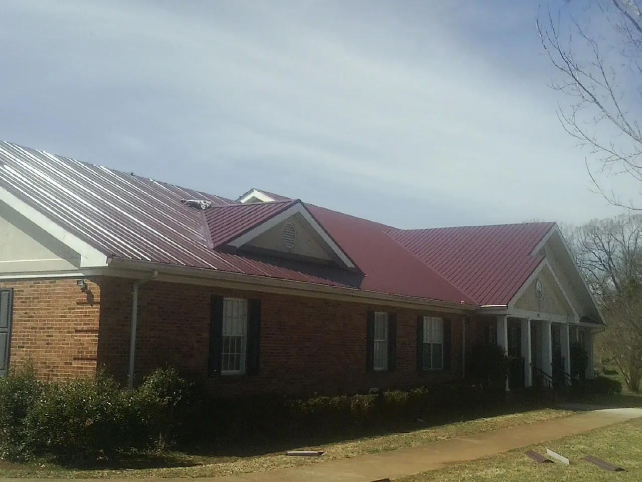 Red metal roof with gabled entries on a long brick building, from a Hail Damage Roof Repair job in El Cajon