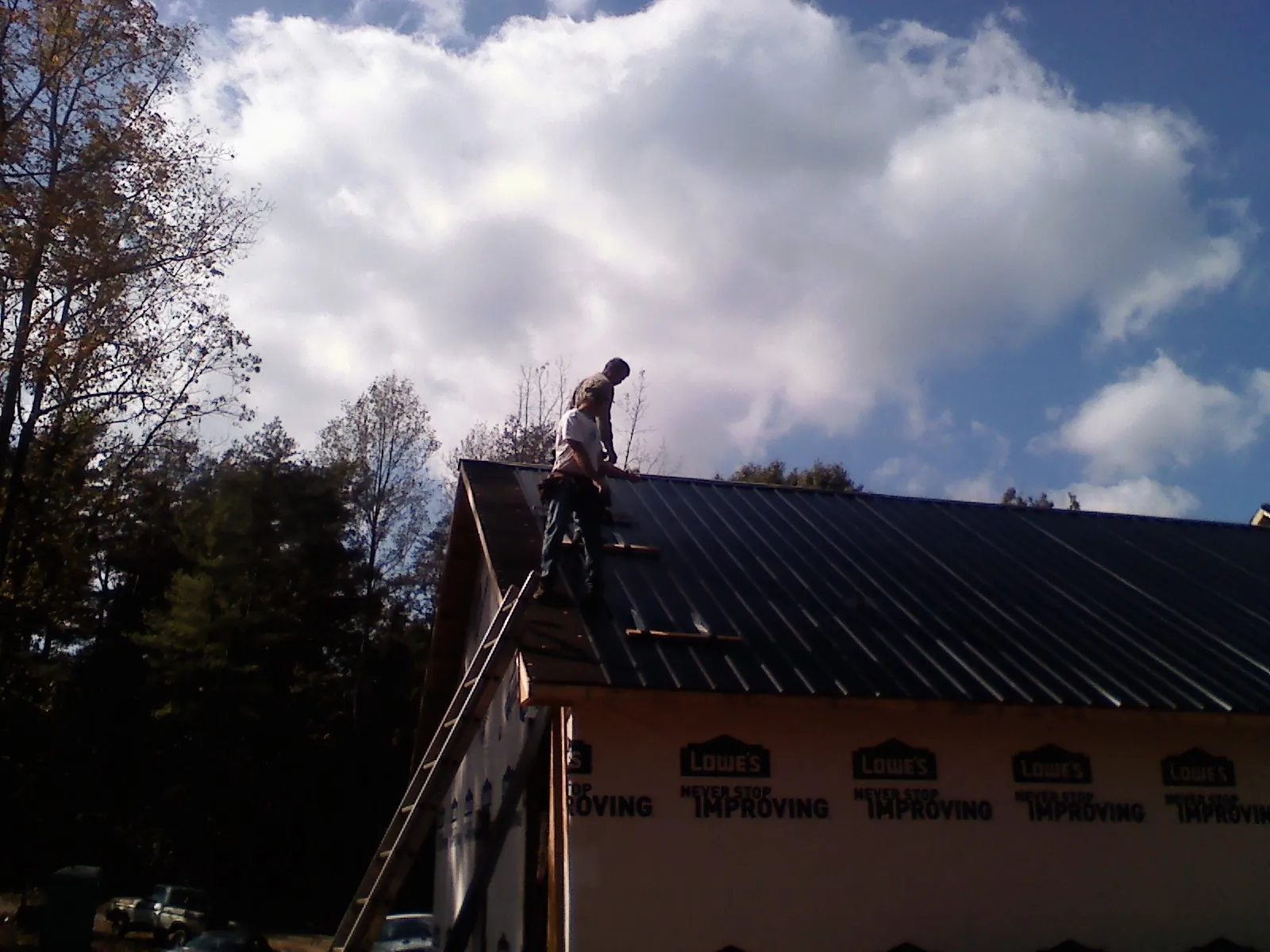 Roofer fastening dark metal panels high against a cloudy sky, from a Roof Inspection job in El Cajon